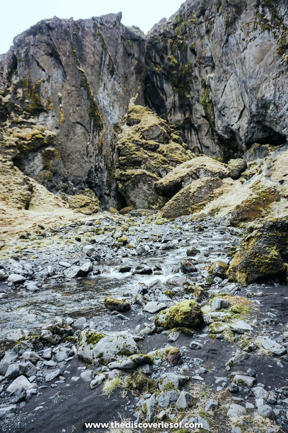 Rocky canyon with towering grey cliffs, moss-covered boulders and a shallow stream on a super jeep day near Þórsmörk