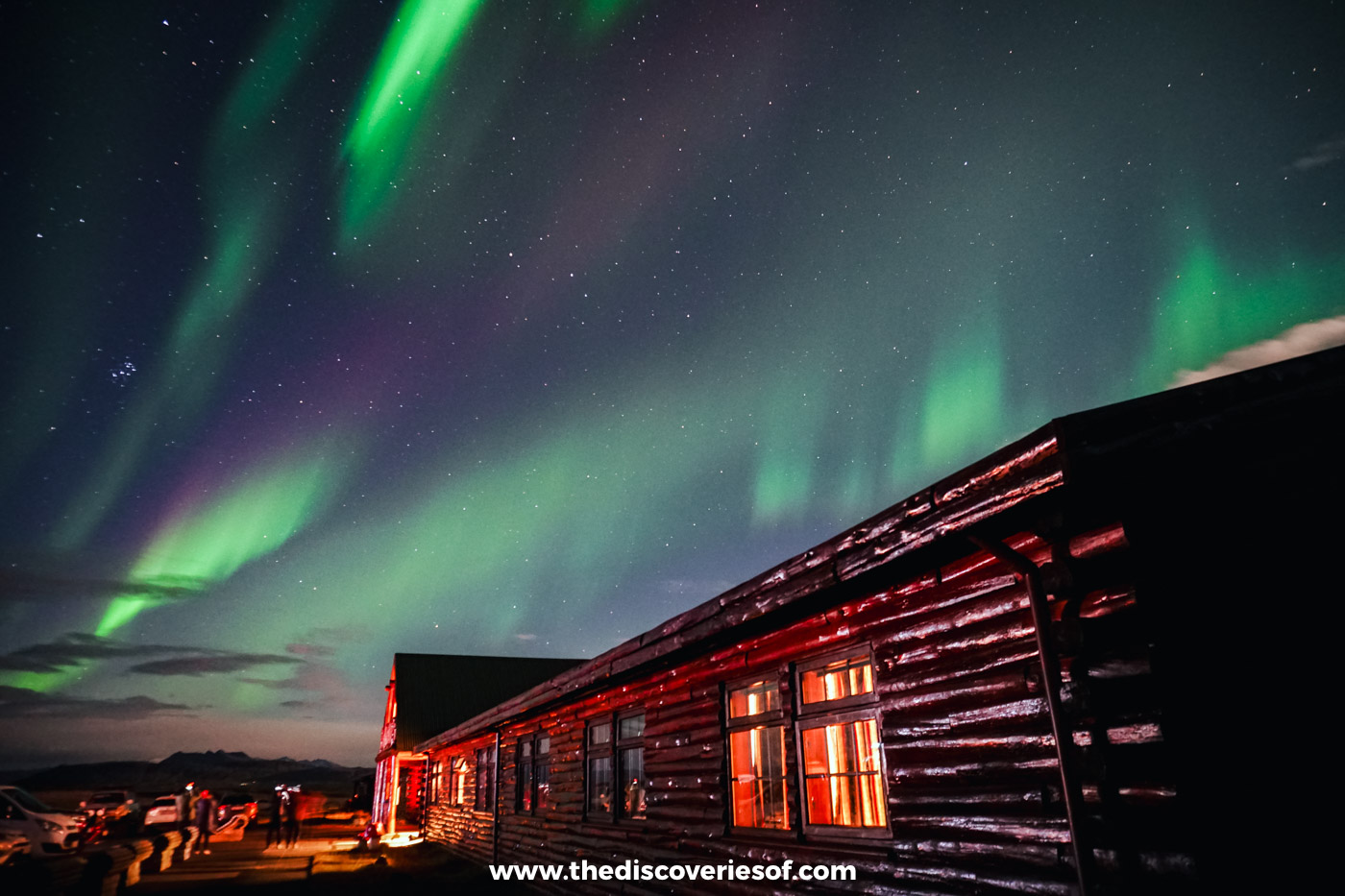 Green and violet Northern Lights swirling above the timber log wing of Hotel Rangá in South Iceland on a September night