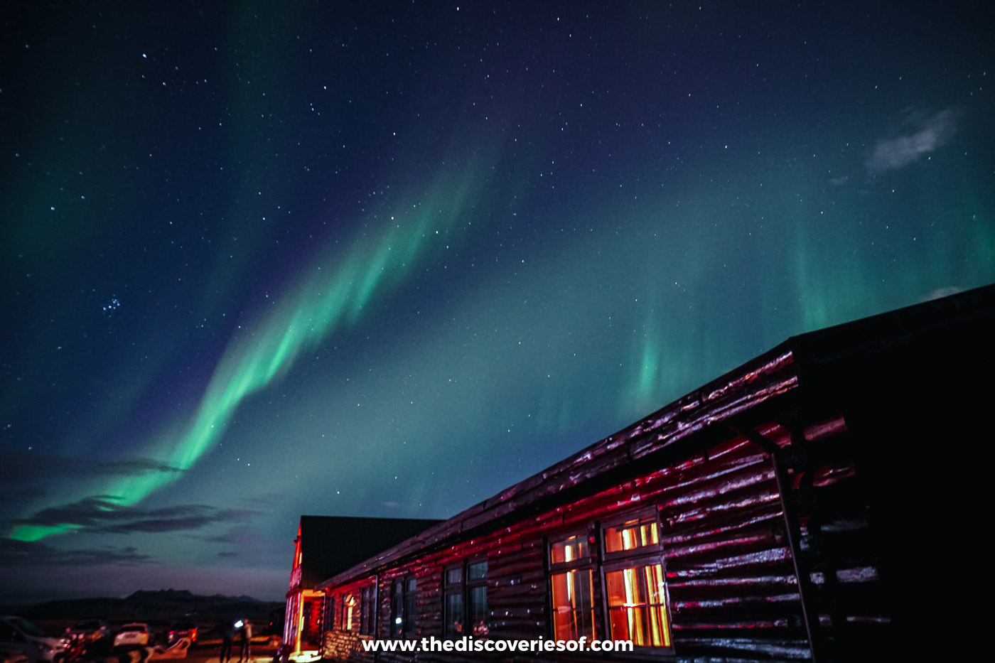 Green Northern Lights curling over the lit log wing of Hotel Rangá near Hella in September
