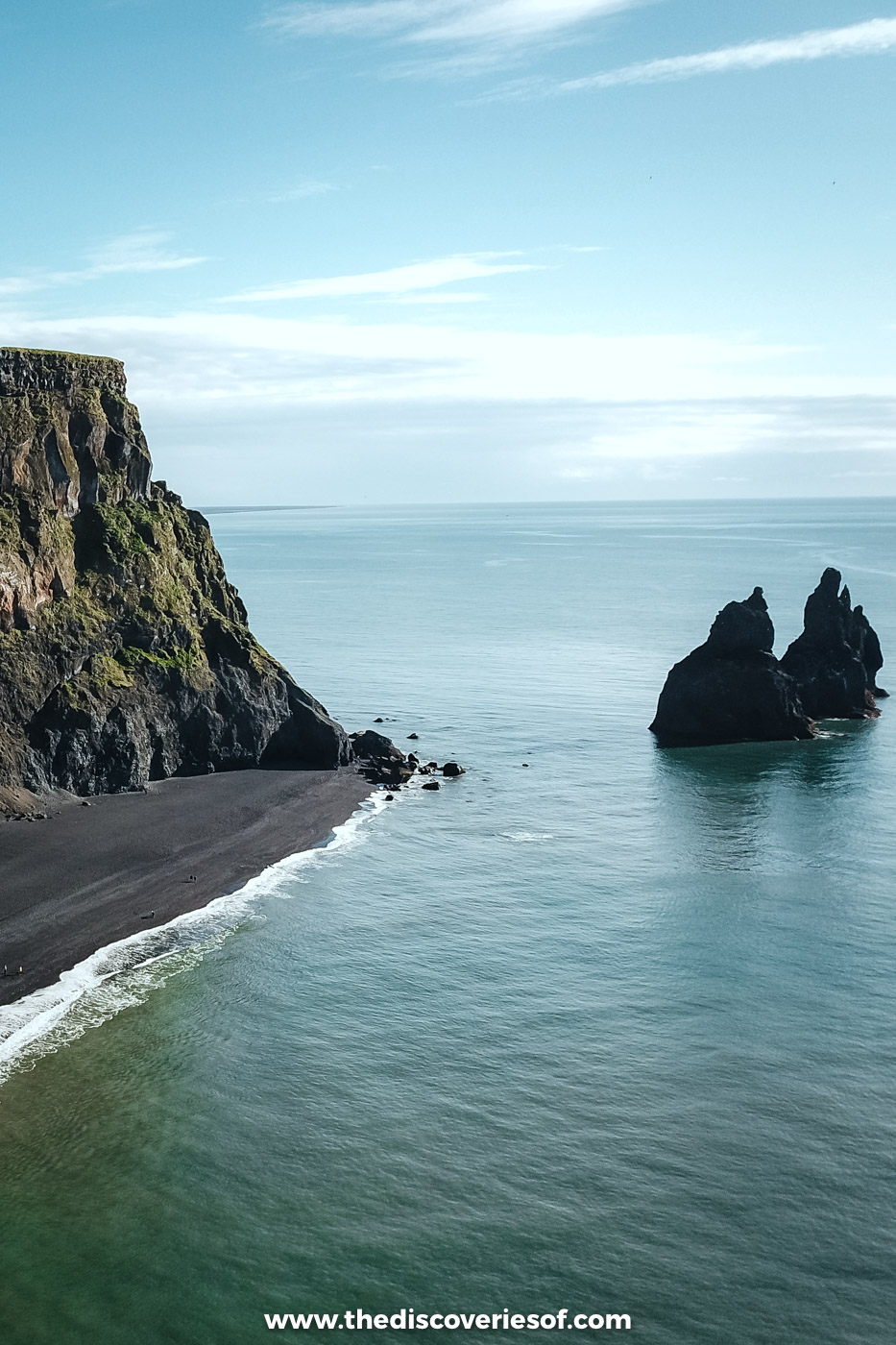 Drone view of the Reynisdrangar sea stacks standing off the tip of Reynisfjall with black sand beside them