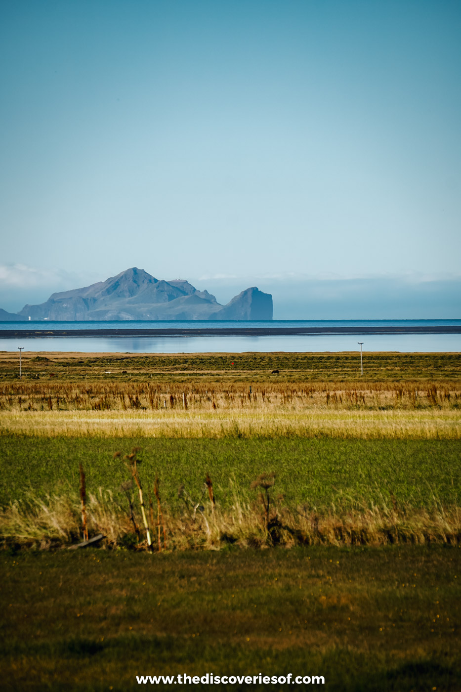 Green farmland on the south coast of Iceland with the Westman Islands rising on the hazy horizon