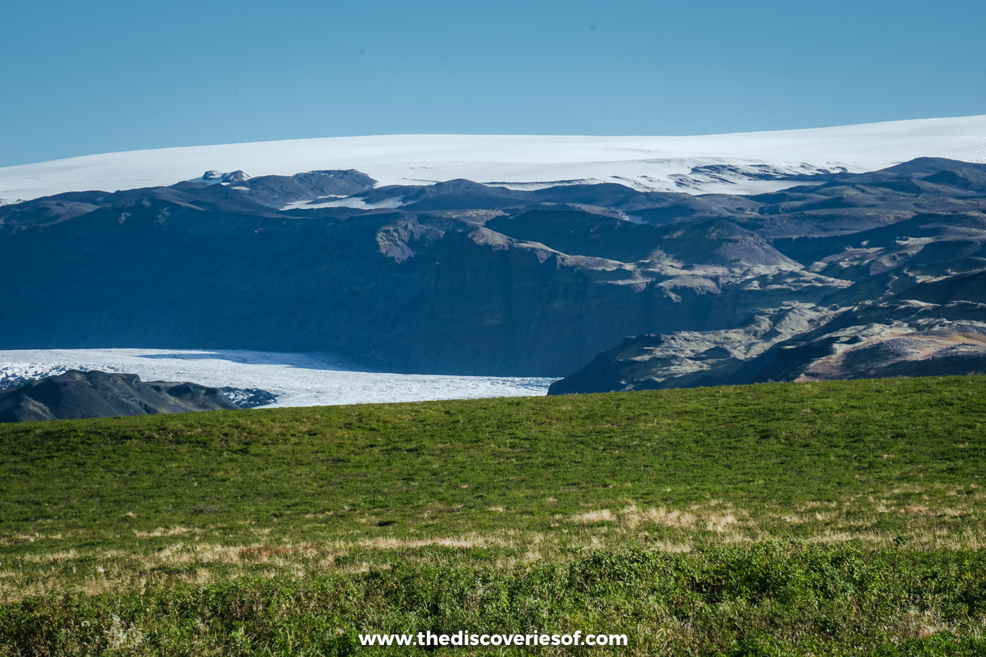 A glacier tongue and snowy ice cap above dark ridges and green pasture on the south coast east of Skógar