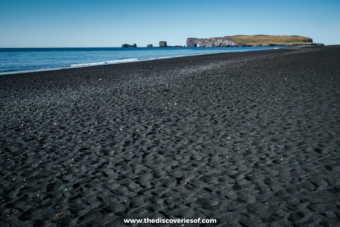 Rippled black sand at Reynisfjara beach stretching towards the sea and the Dyrhólaey headland on the horizon