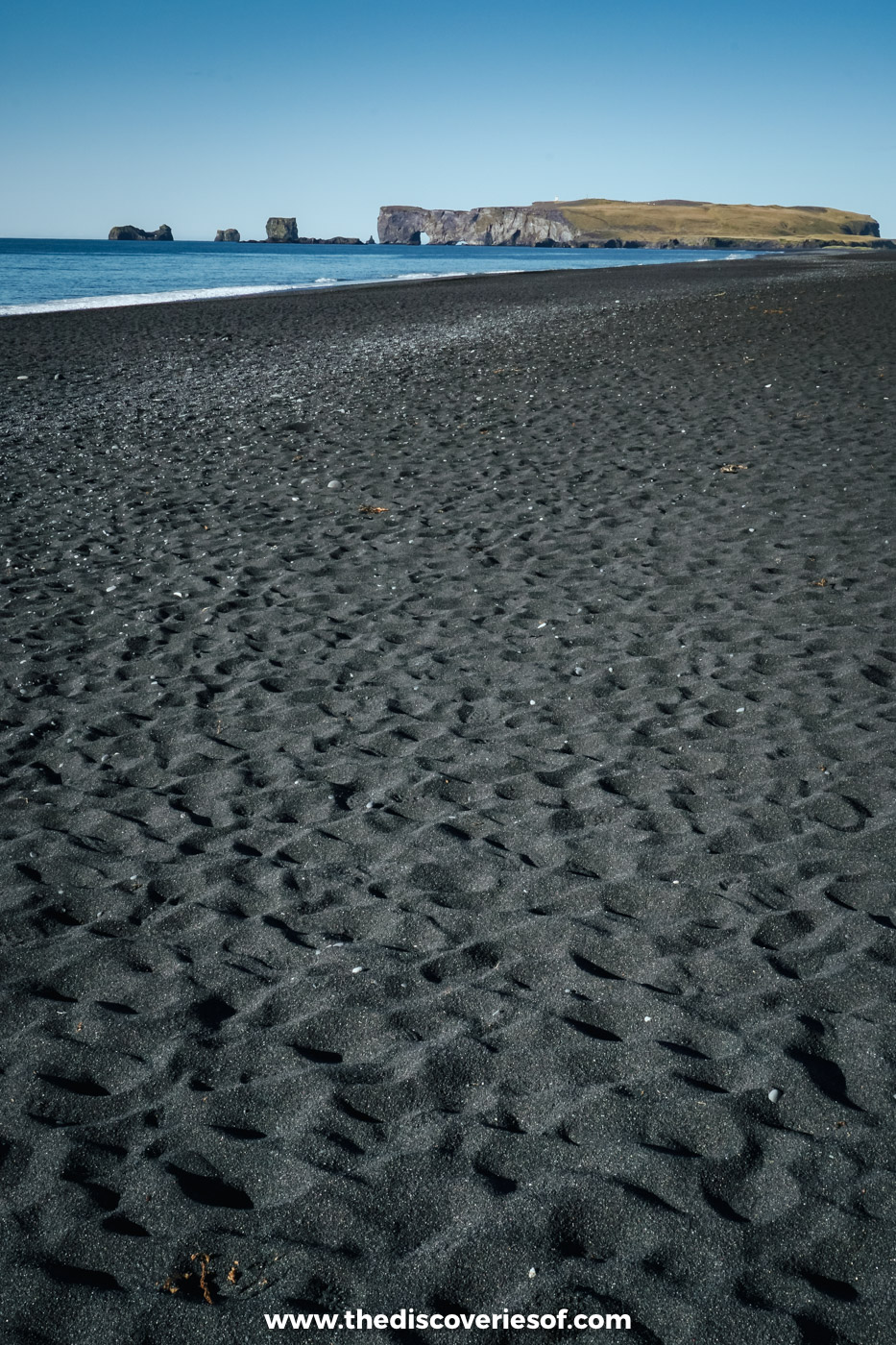 Rippled black sand at Reynisfjara stretching towards the Dyrhólaey headland under a clear blue sky