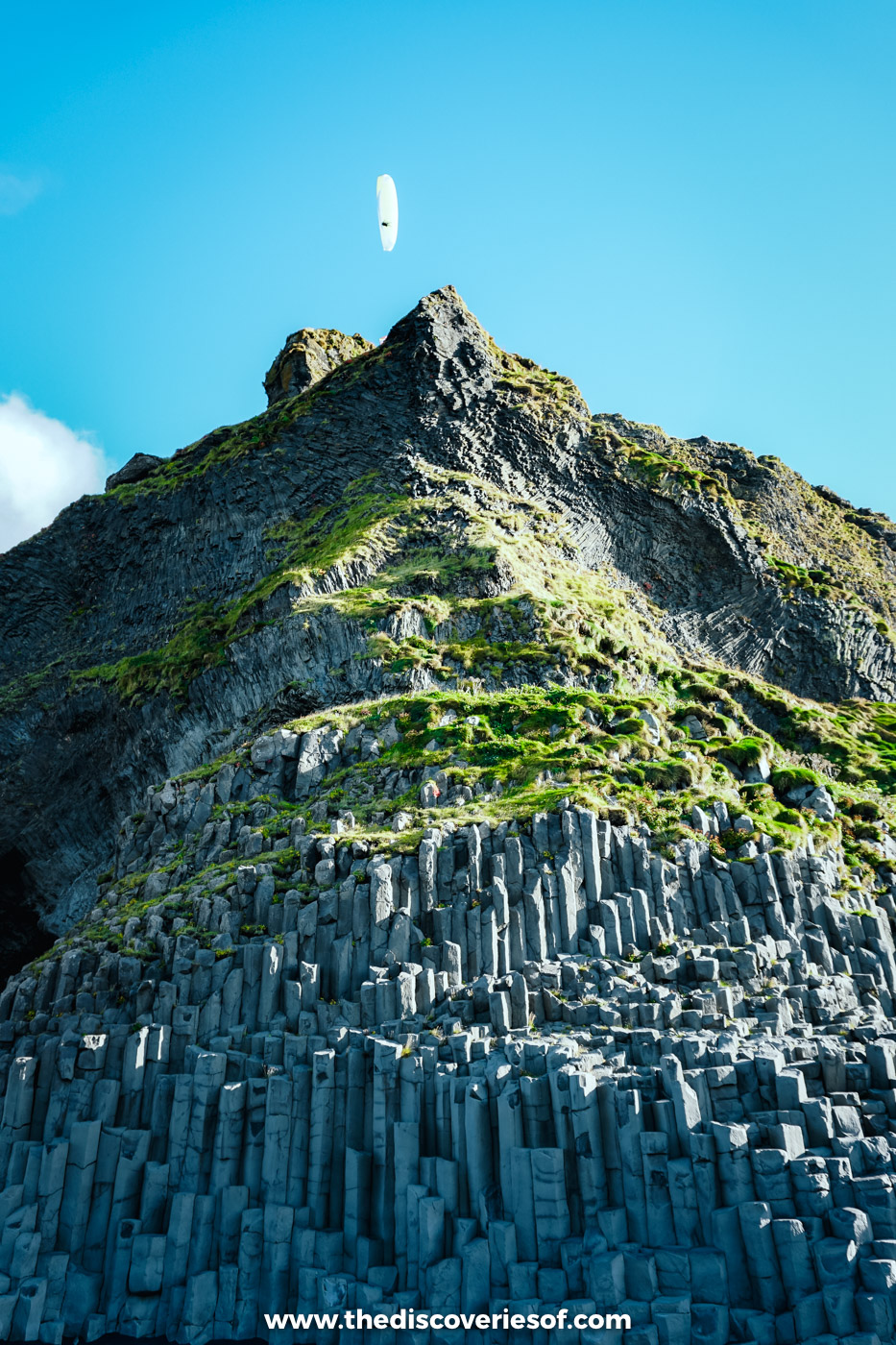 Hexagonal basalt columns rising up the cliff at Reynisfjara with a paraglider in the blue sky above