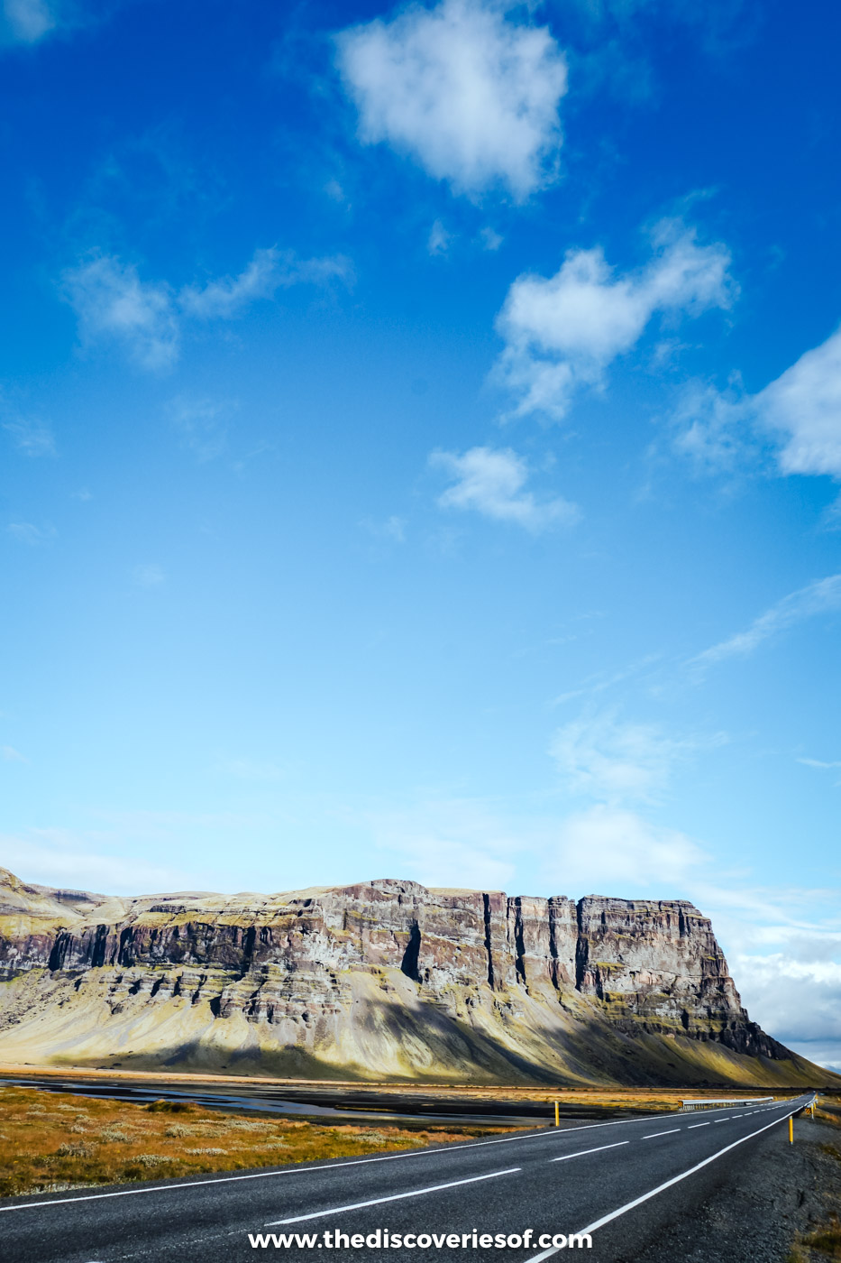 The empty Ring Road running straight towards a long flat-topped cliff under a bright blue September sky in south east Iceland