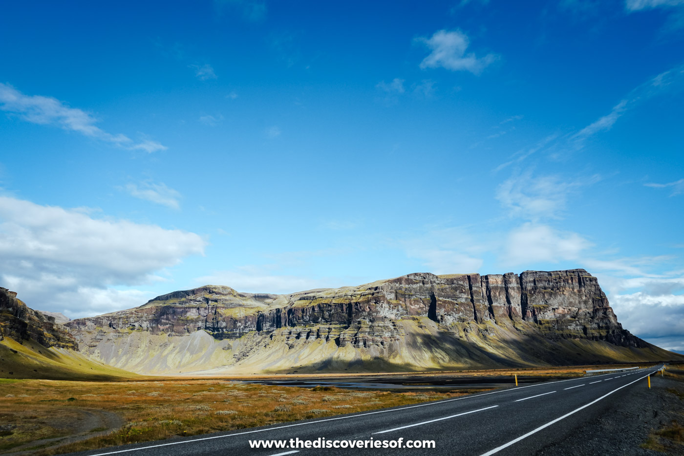 The Ring Road running towards a long flat-topped cliff under blue sky on Iceland's south coast in September