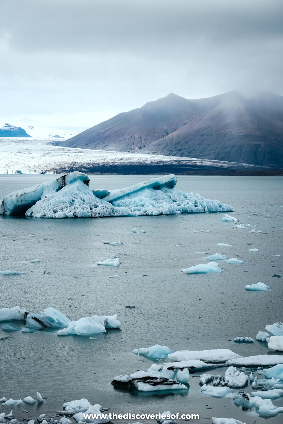 Pale blue icebergs floating on Jökulsárlón glacier lagoon with the glacier and a dark mountain behind