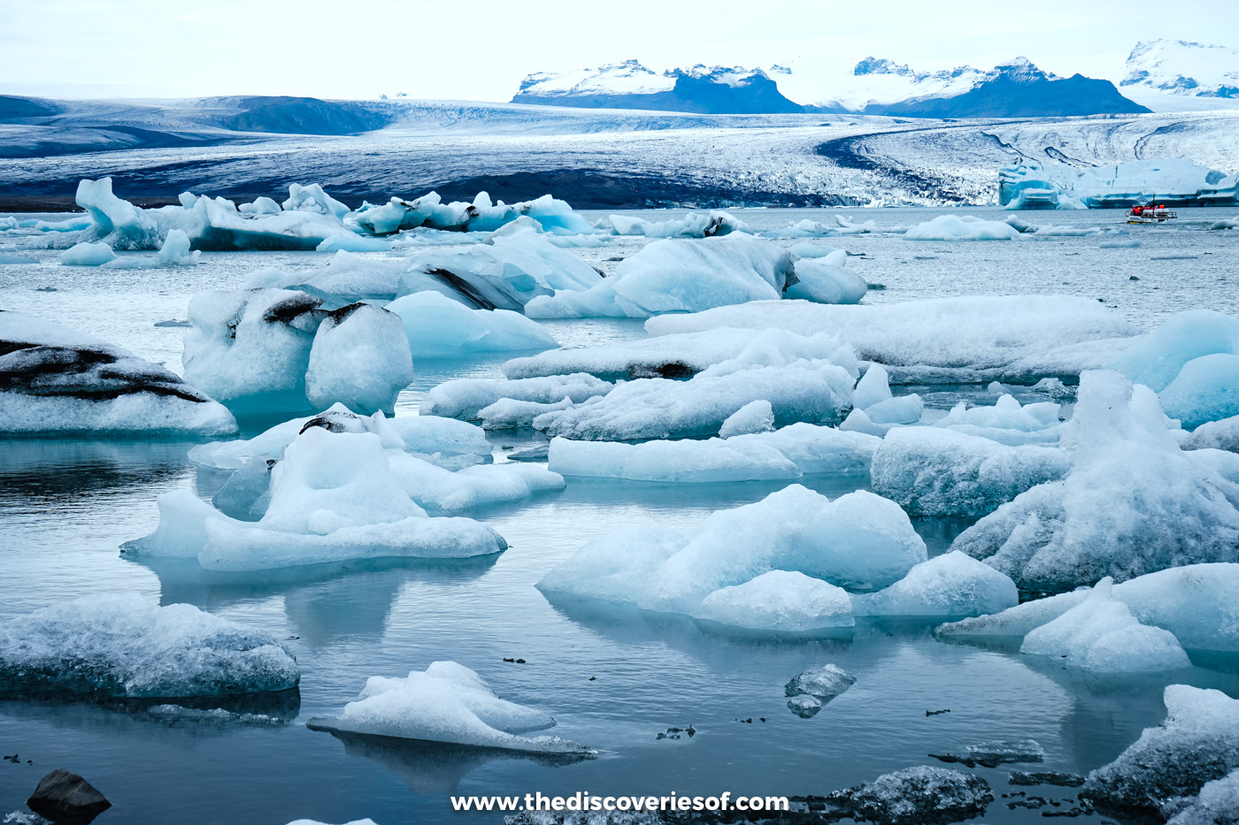 White and blue icebergs crowding the shore of Jökulsárlón glacier lagoon with mountains and cloud behind
