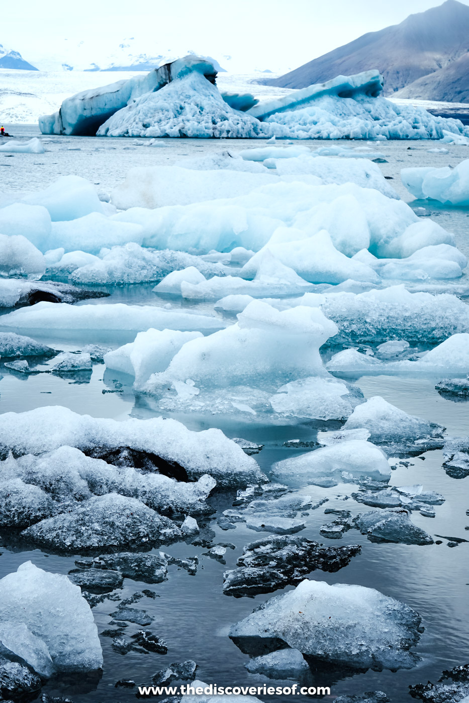 Blue and white icebergs floating close to the shore of Jökulsárlón glacier lagoon under a grey September sky