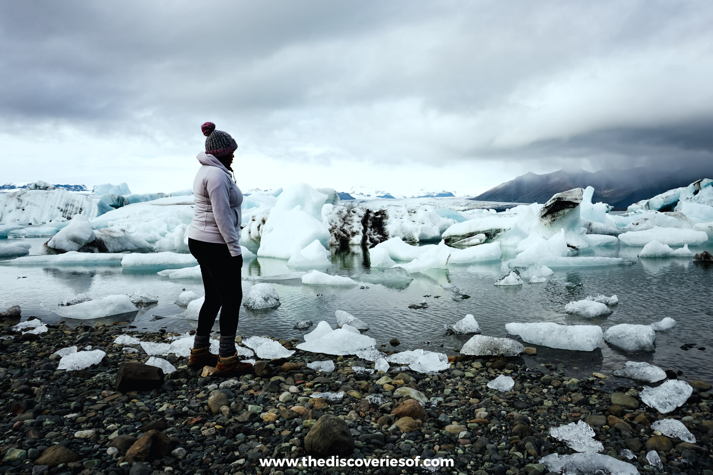 Julianna in a white jacket among stranded icebergs on the shore of Jökulsárlón glacier lagoon