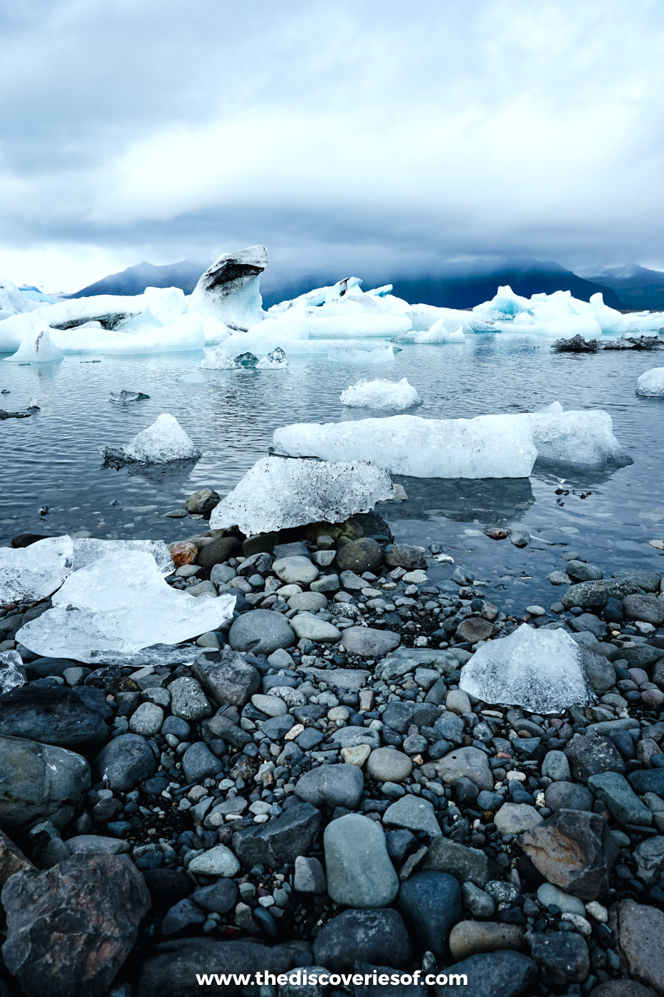 Chunks of white and blue ice resting on dark stones at the edge of Jökulsárlón glacier lagoon, south-east Iceland