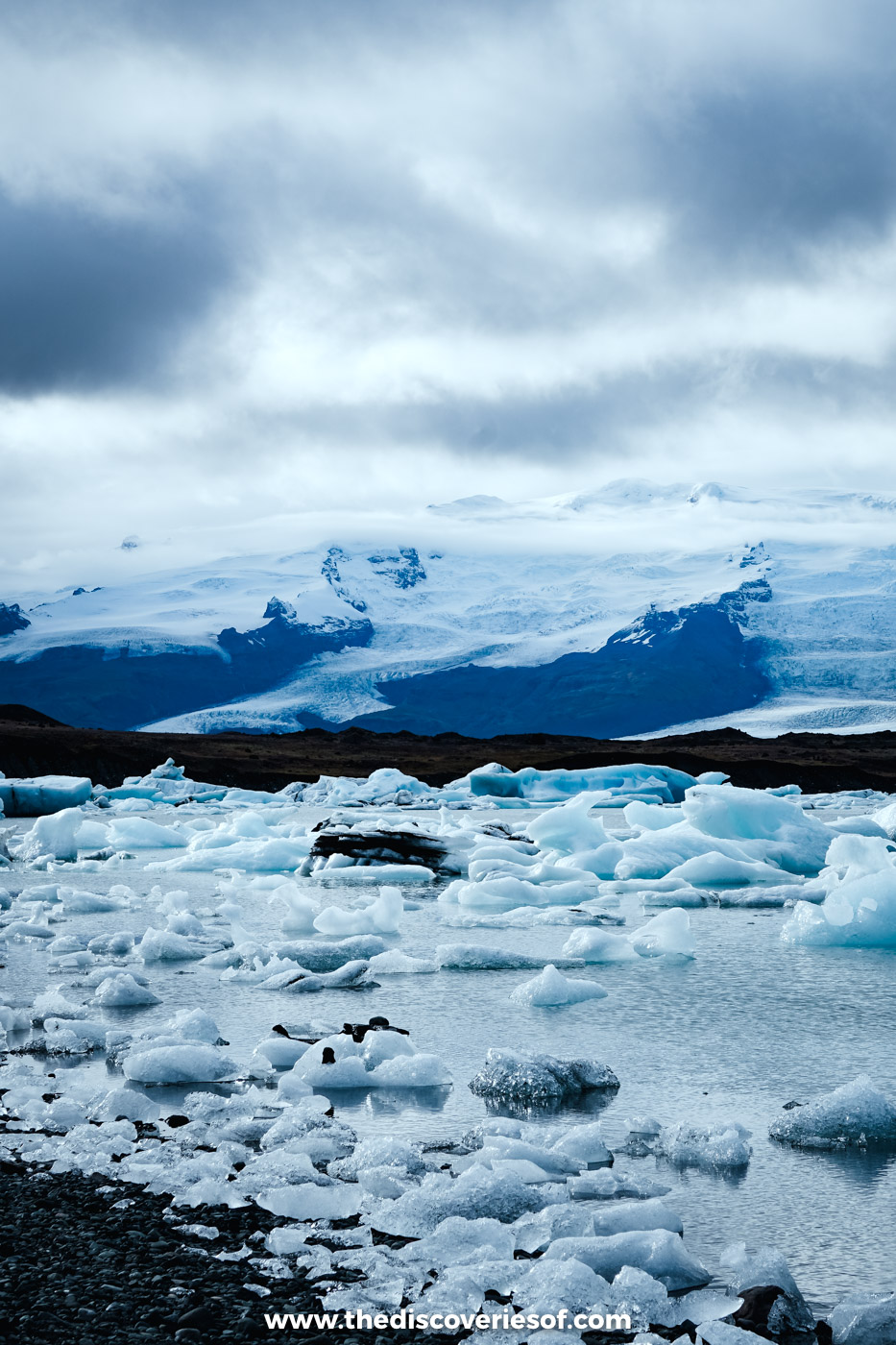 Icebergs crowding the stony shore of Jökulsárlón glacier lagoon below the glacier and a heavy grey September sky