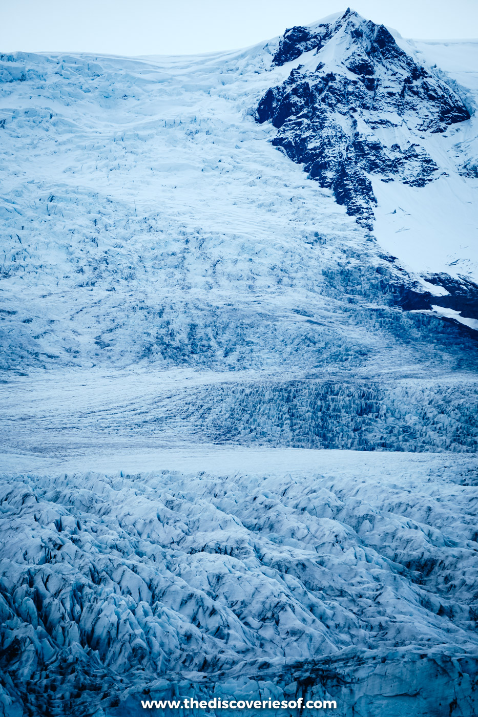 Crevassed blue-white tongue of Fjallsjökull glacier descending from a snowy peak towards Fjallsárlón