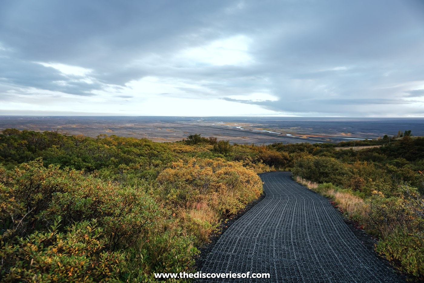 Matted walking path through orange and green autumn scrub on the heath above Skaftafell, with the sandur plain beyond