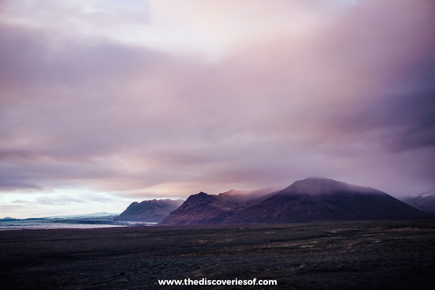 Pink evening light over dark mountains and the flat black sandur beside the Ring Road