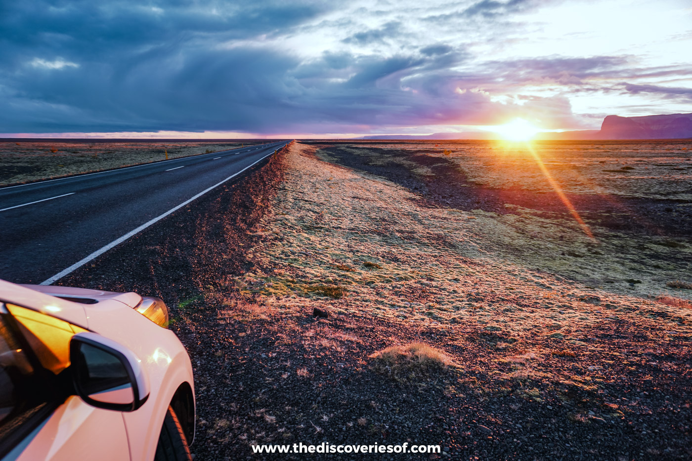 Sunset over a straight stretch of the Ring Road with a hire car's wing mirror in the foreground