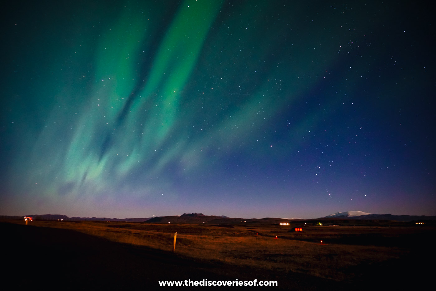 Green ribbons of the Northern Lights filling a starry sky over the dark countryside near Hella