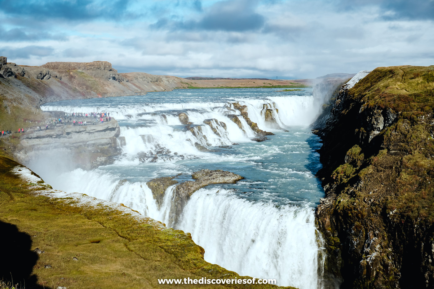 Visitors on the rocky shelf of the lower path beside the upper cascade of Gullfoss, canyon to the right