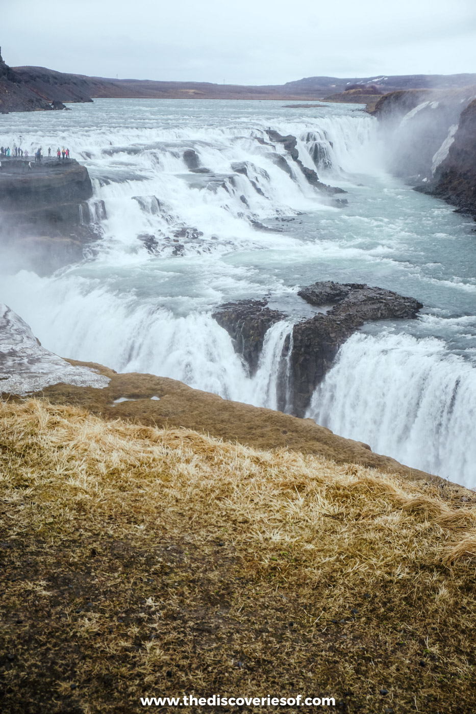 The upper tier of Gullfoss tumbling over rock ledges into the Hvítá canyon under grey May skies