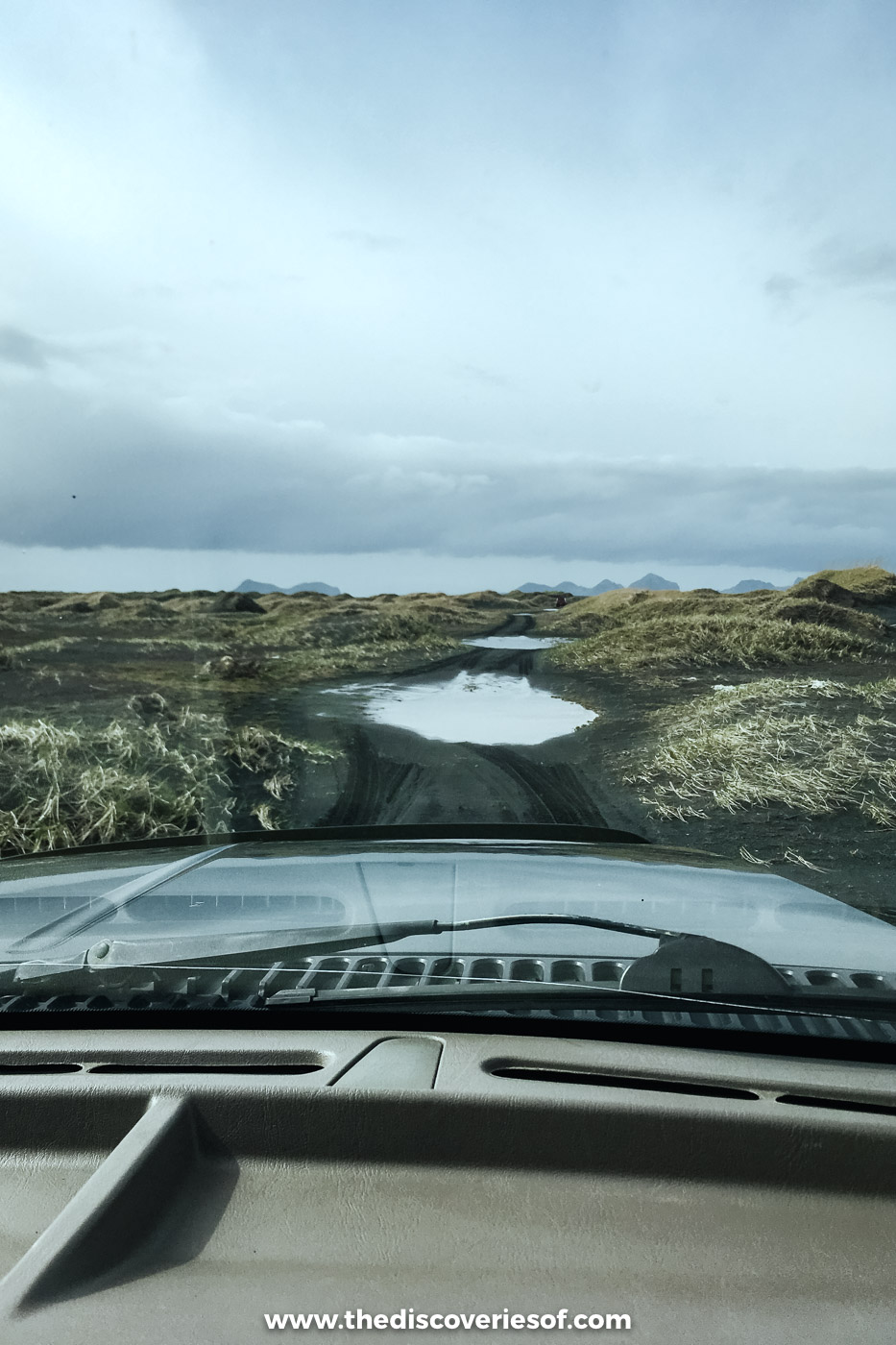 A super jeep dashboard and windscreen looking out over a flooded track across black sand and moss on the south coast in May