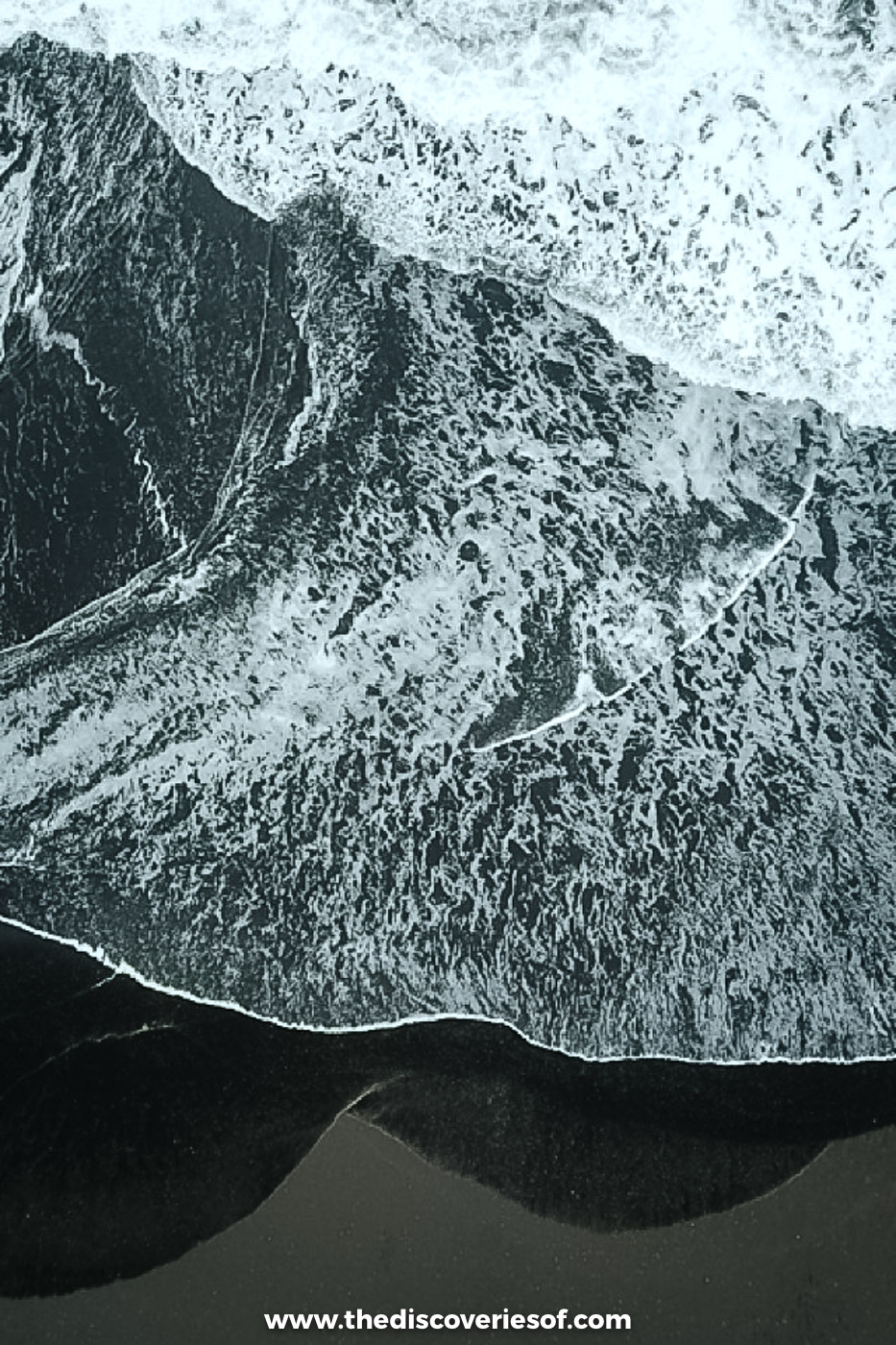Drone shot of white surf breaking in lacy patterns on the black sand beach at Landeyjafjara