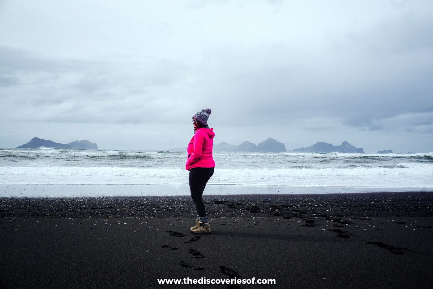 Julianna in a pink jacket standing on a wide black sand beach looking out to sea near Landeyjahöfn