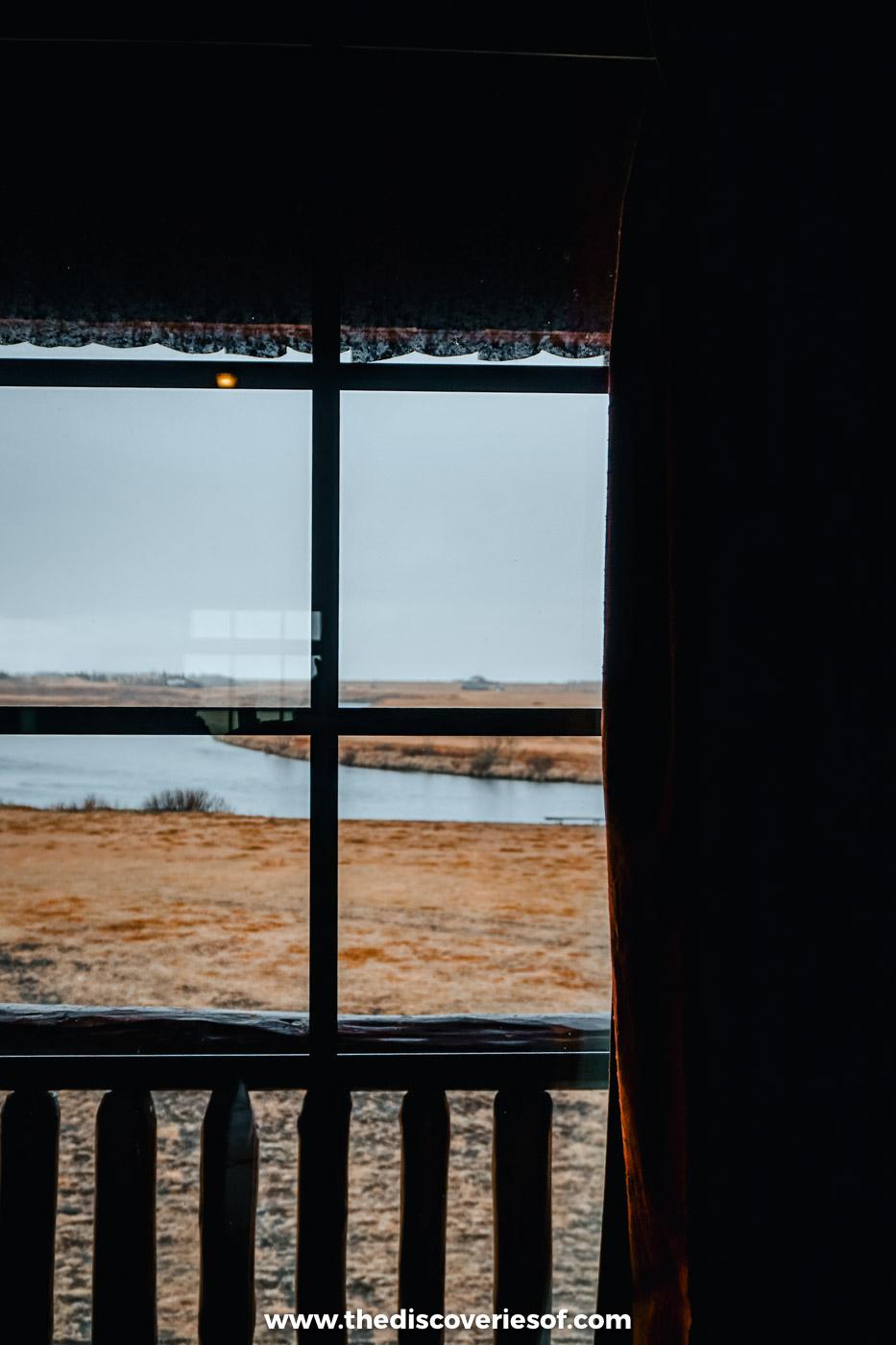 Looking out of a dark hotel room window over a wooden balcony to flat moorland at Hotel Rangá