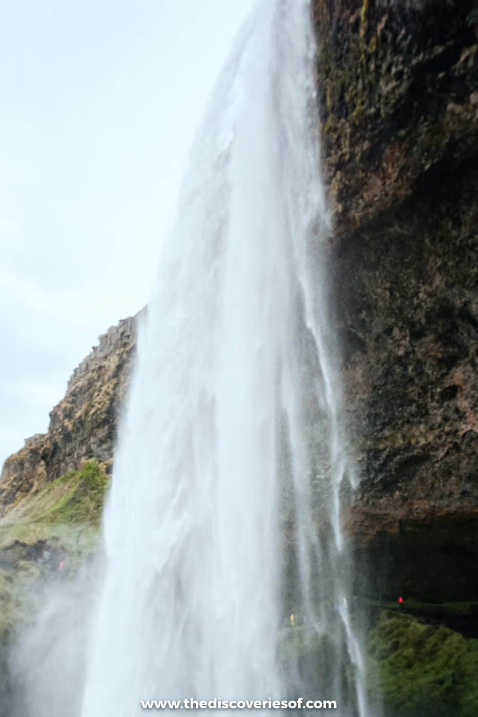 Seljalandsfoss seen side-on from the path, the water falling past the dark overhanging rock