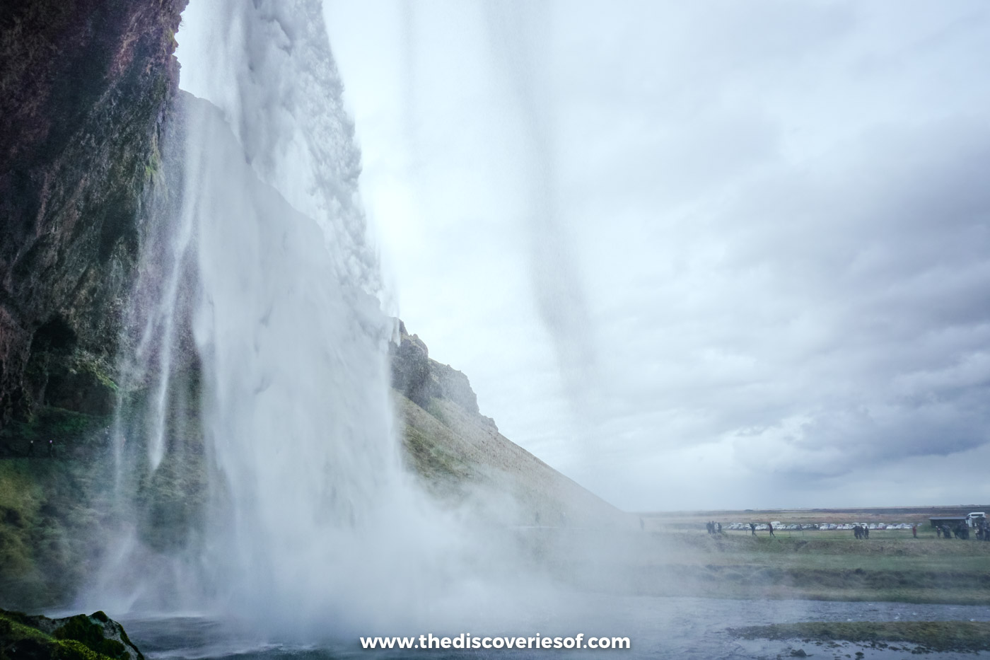 View from the path behind Seljalandsfoss, looking through the falling water to the flat plain beyond