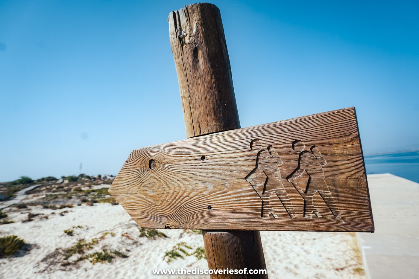 A carved wooden walkers' signpost on a post in the dunes of Ilha Deserta, under a clear blue sky