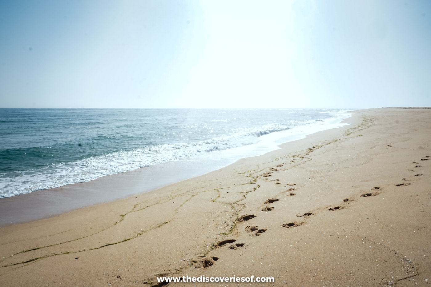Footprints in the sand along an empty stretch of the ocean beach on Ilha Deserta, with waves rolling in under a hazy sky