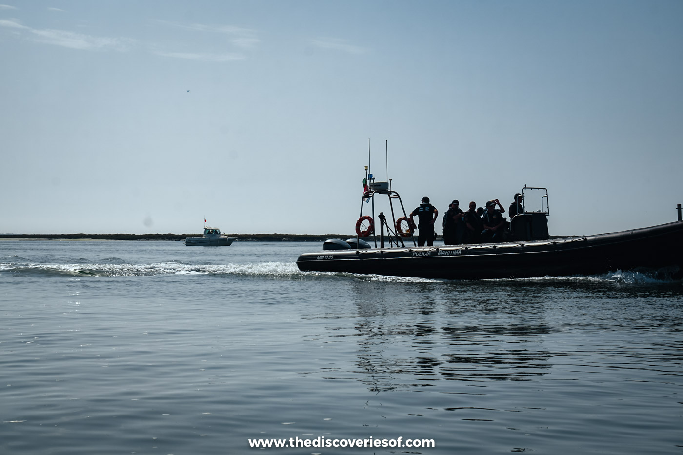 A small open boat carrying a group of passengers across the calm water of the Ria Formosa lagoon