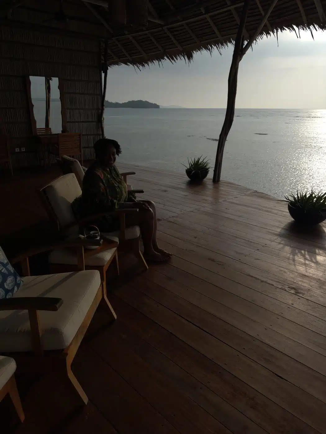 Julianna relaxing in an armchair on the spa deck at Papua Paradise, with a teapot beside her and the calm sea beyond