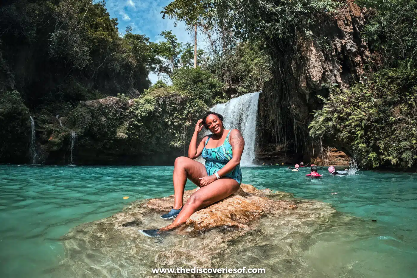 Julianna sitting on a rock in the turquoise pool below the tiered cascade of Kawasan Falls, Badian, Cebu
