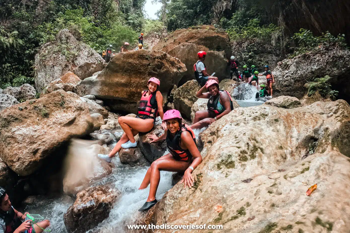 Canyoneers in helmets and life jackets scrambling over boulders beside a small cascade in the Badian canyon, Cebu
