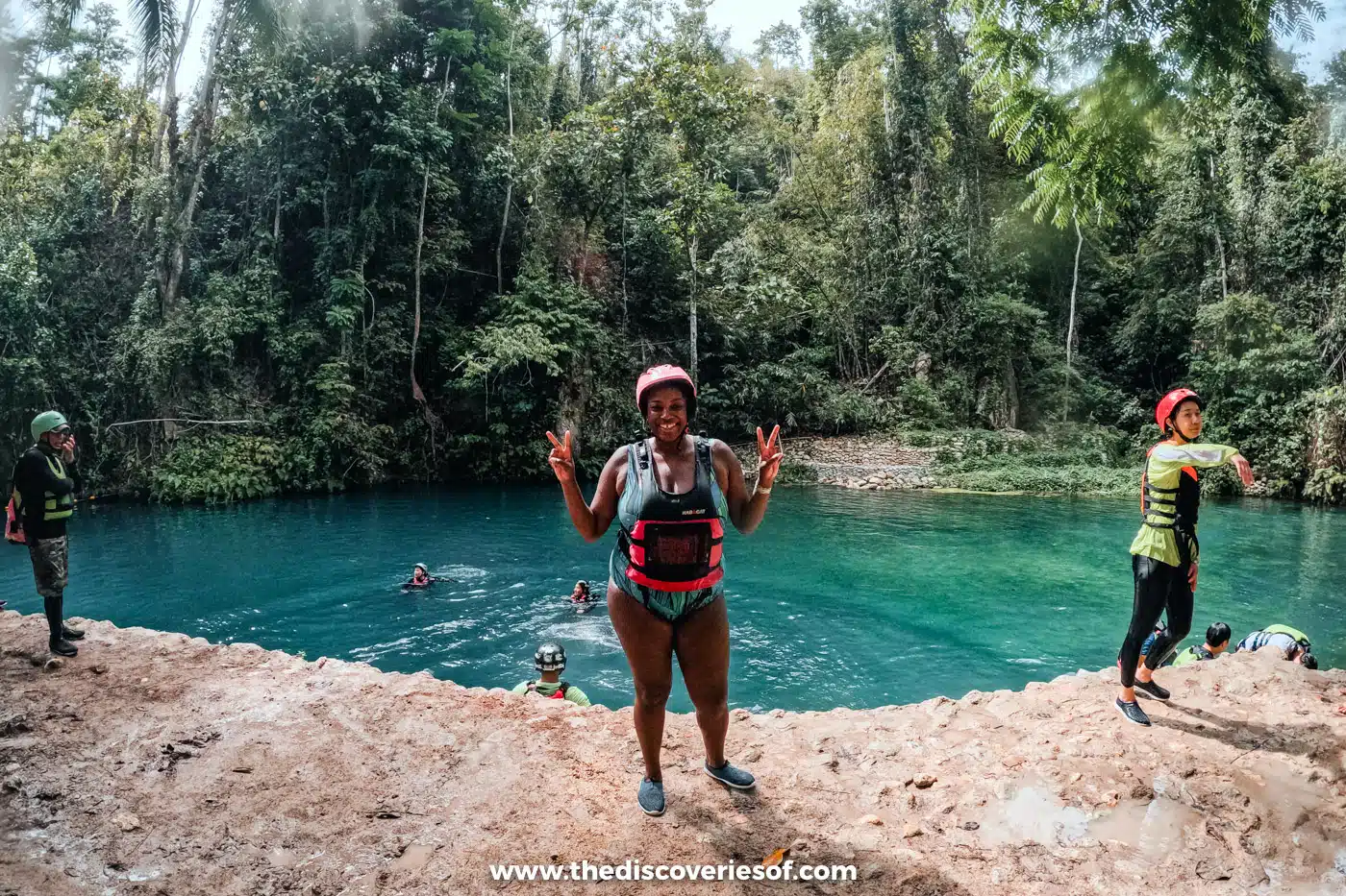 Julianna in a helmet and life jacket on a rocky ledge above a turquoise jungle pool, canyoneering to Kawasan Falls