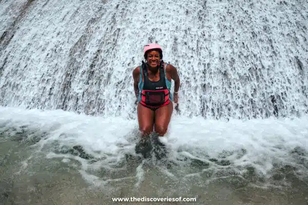 Julianna in a helmet and life jacket sitting in a white cascade of water while canyoneering near Kawasan Falls, Cebu