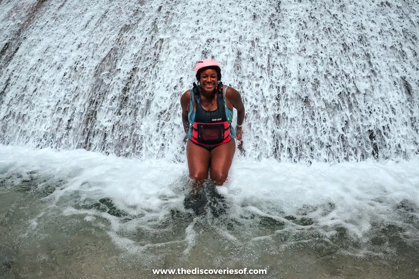 Julianna in a helmet and life jacket sitting in a white cascade of water while canyoneering near Kawasan Falls, Cebu