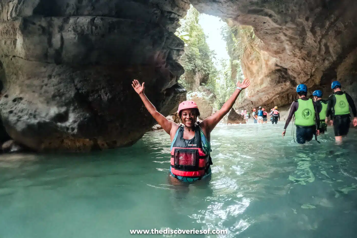 Julianna raising her arms in a turquoise pool at the mouth of a rocky gorge while canyoneering to Kawasan Falls, Cebu