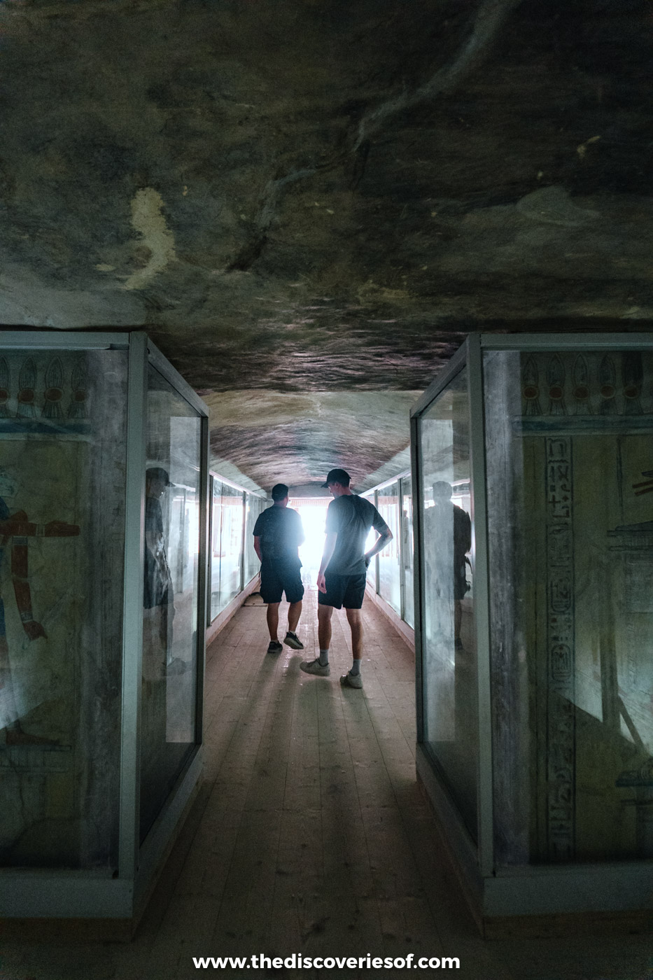 Two visitors silhouetted in the corridor of the tomb of Khaemwaset, its painted walls behind glass