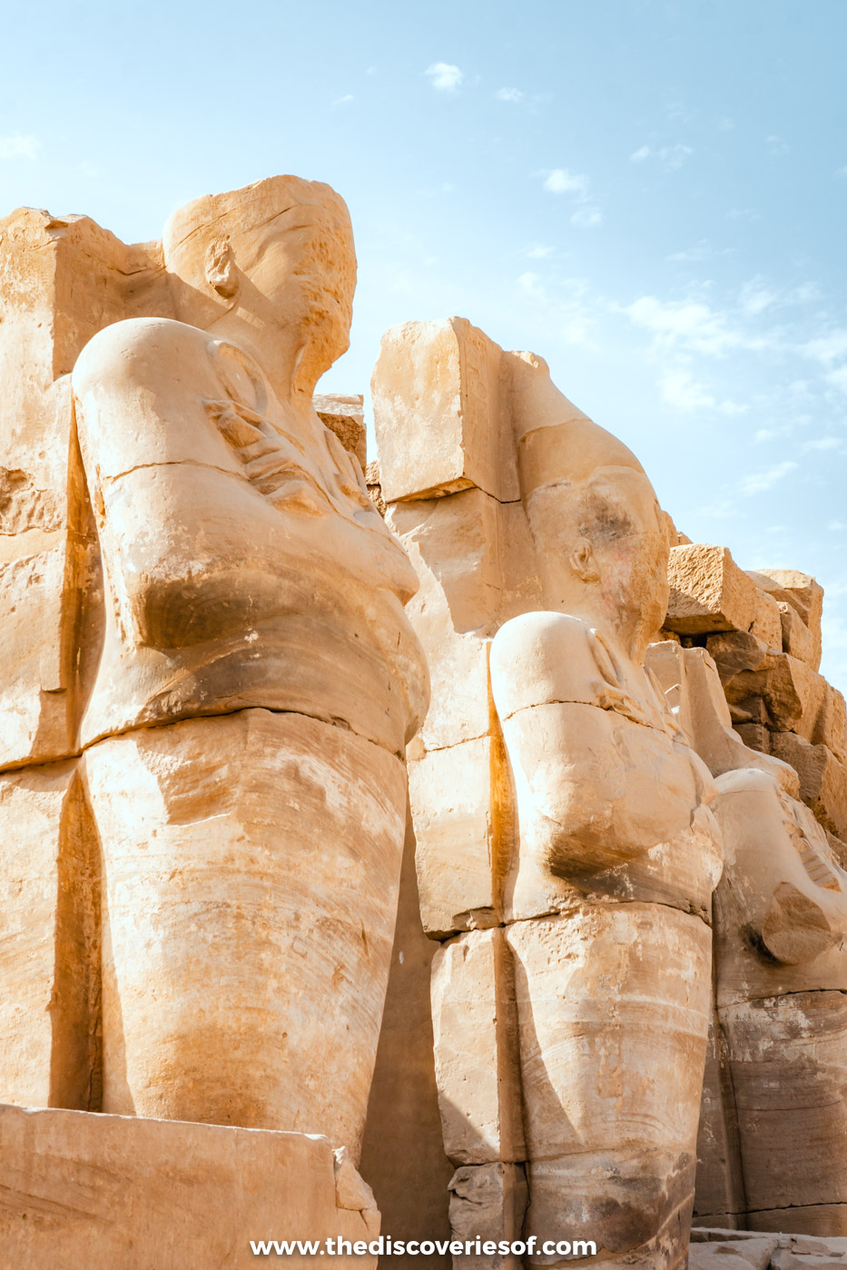 A row of weathered Osiride statues of the pharaoh against a blue sky at Karnak Temple in Luxor