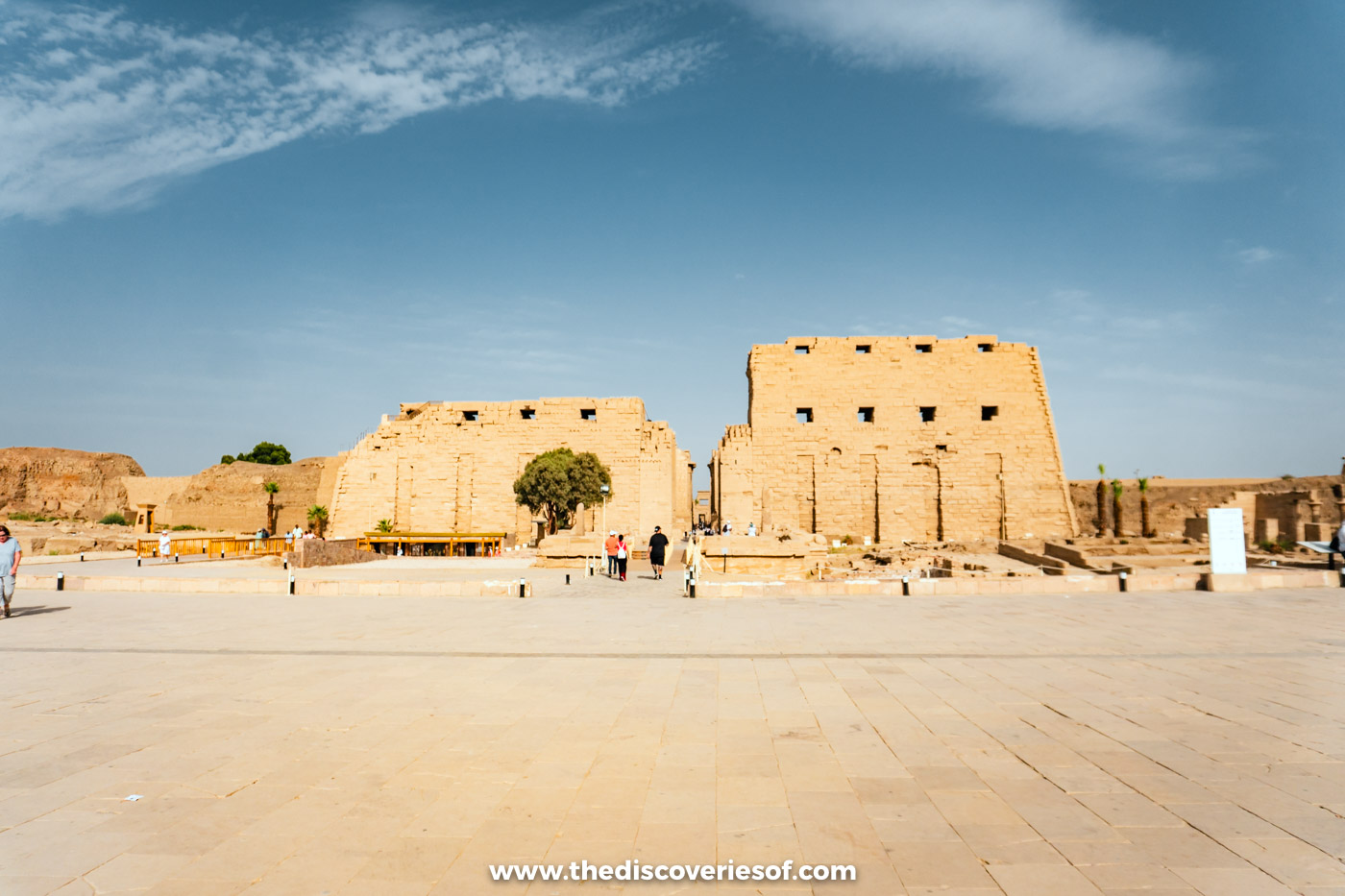 The broad unfinished first pylon of Karnak Temple across a wide paved forecourt under a blue sky, Luxor