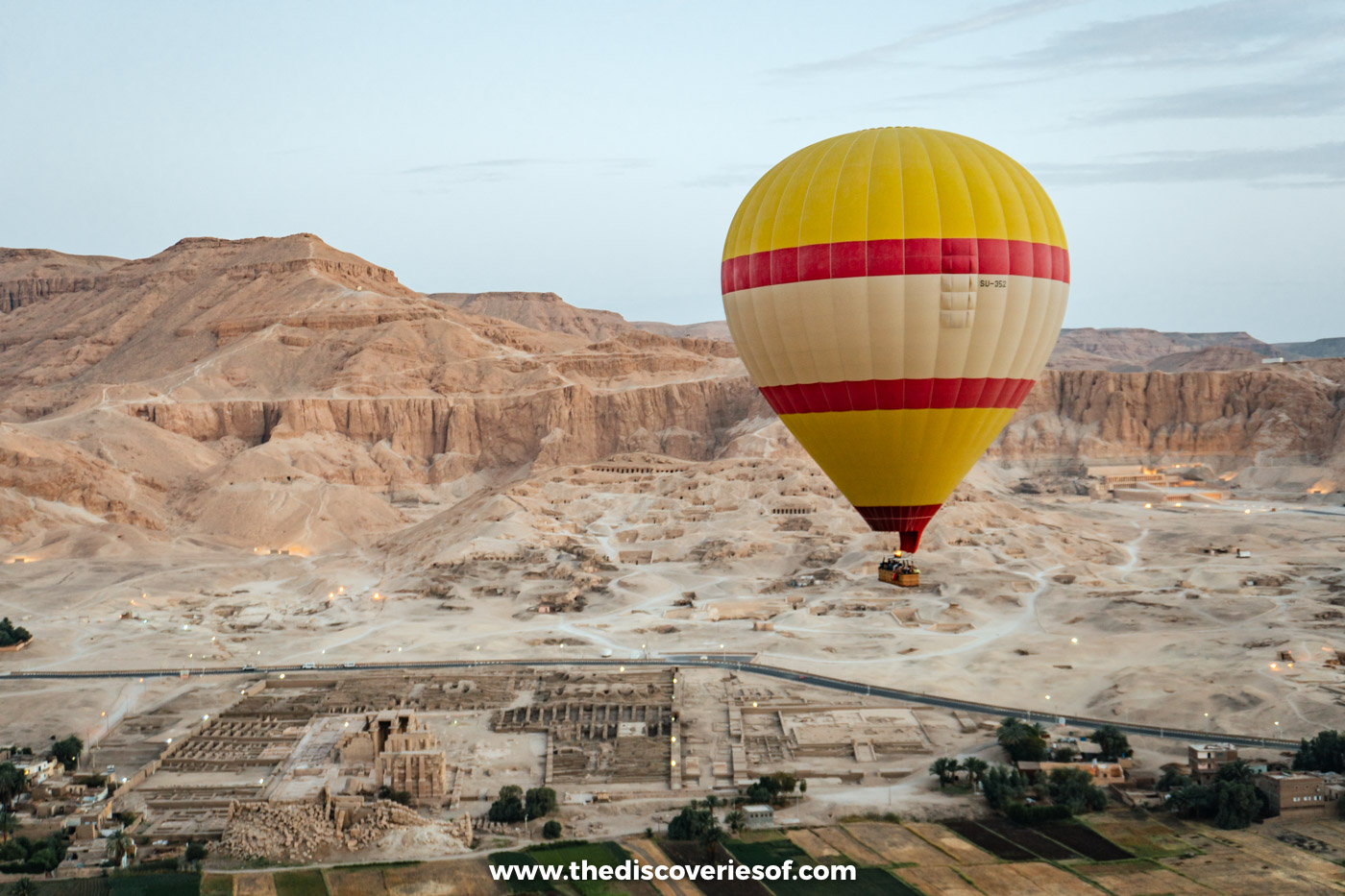 Hot air balloon above West Bank temple ruins and fields with the Theban cliffs behind, Luxor
