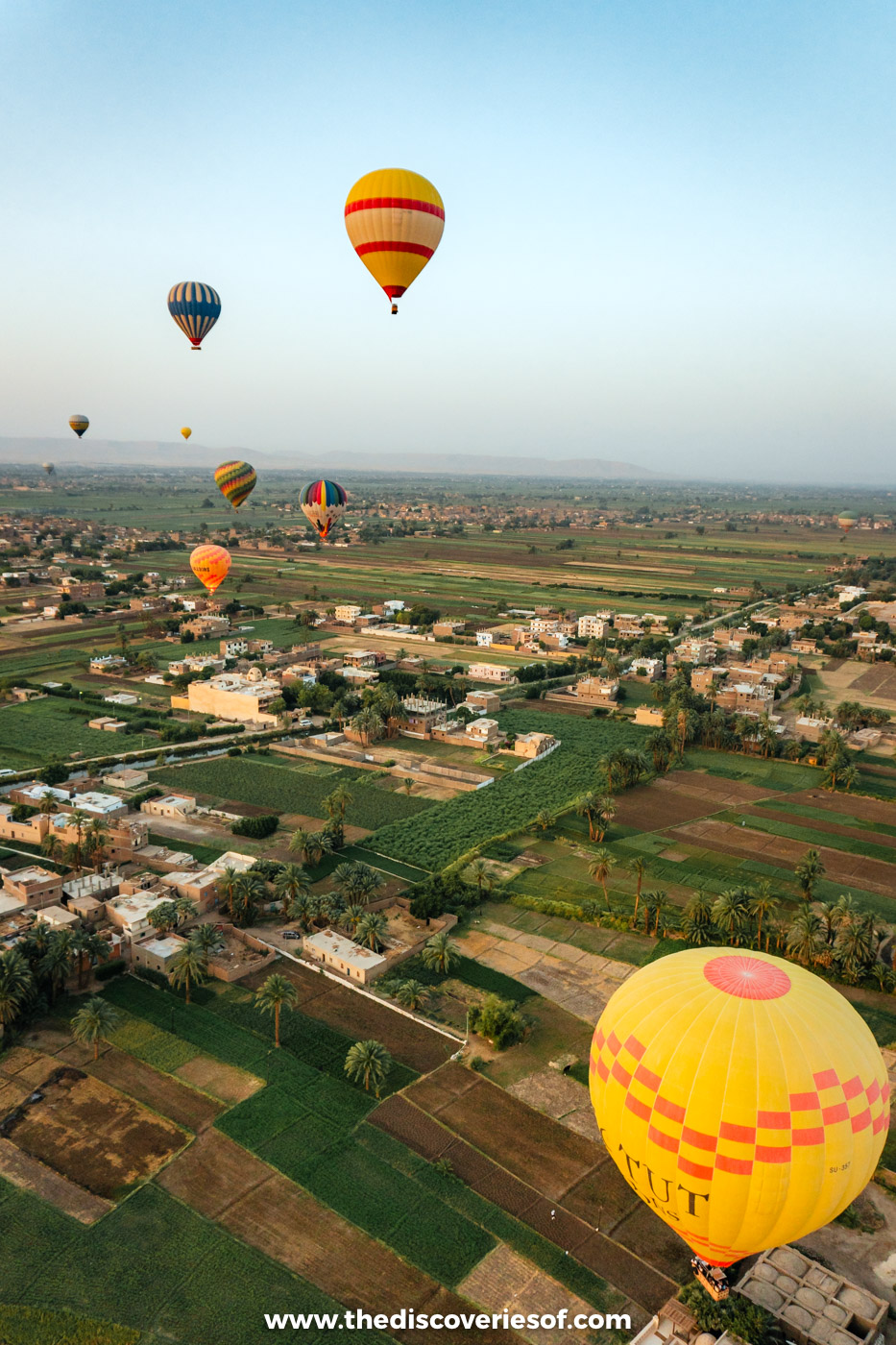 Hot air balloons drifting low over a village and fields on the West Bank of Luxor at sunrise