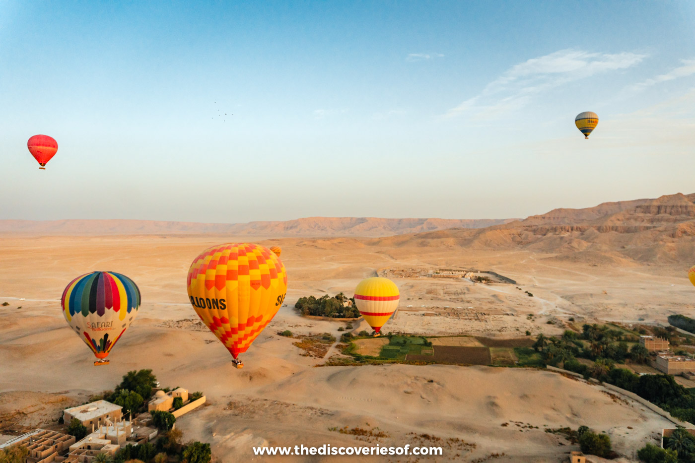 Colourful hot air balloons drifting low over the desert edge and fields of Luxor's West Bank at sunrise