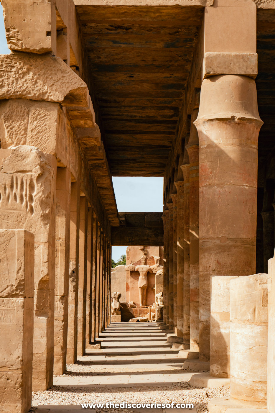 Long shaded colonnade of sandstone pillars leading to a statue at the far end, Karnak Temple, Luxor