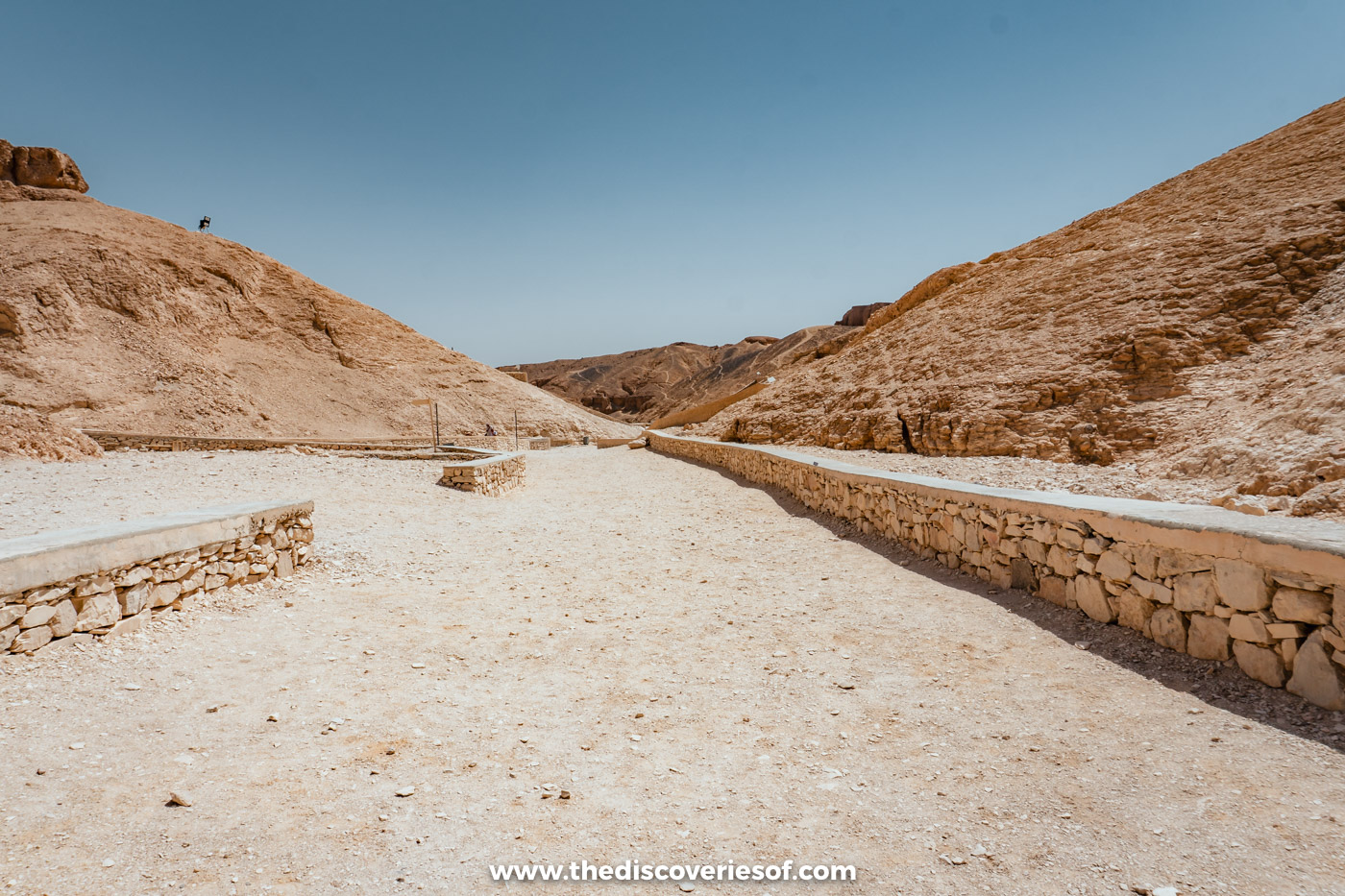 Paved path with low stone walls running between desert hills in the Valley of the Kings, Luxor