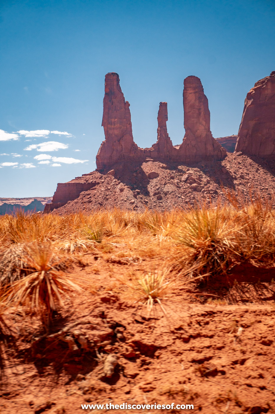 The Three Sisters spires above desert grasses on the Valley Drive in Monument Valley