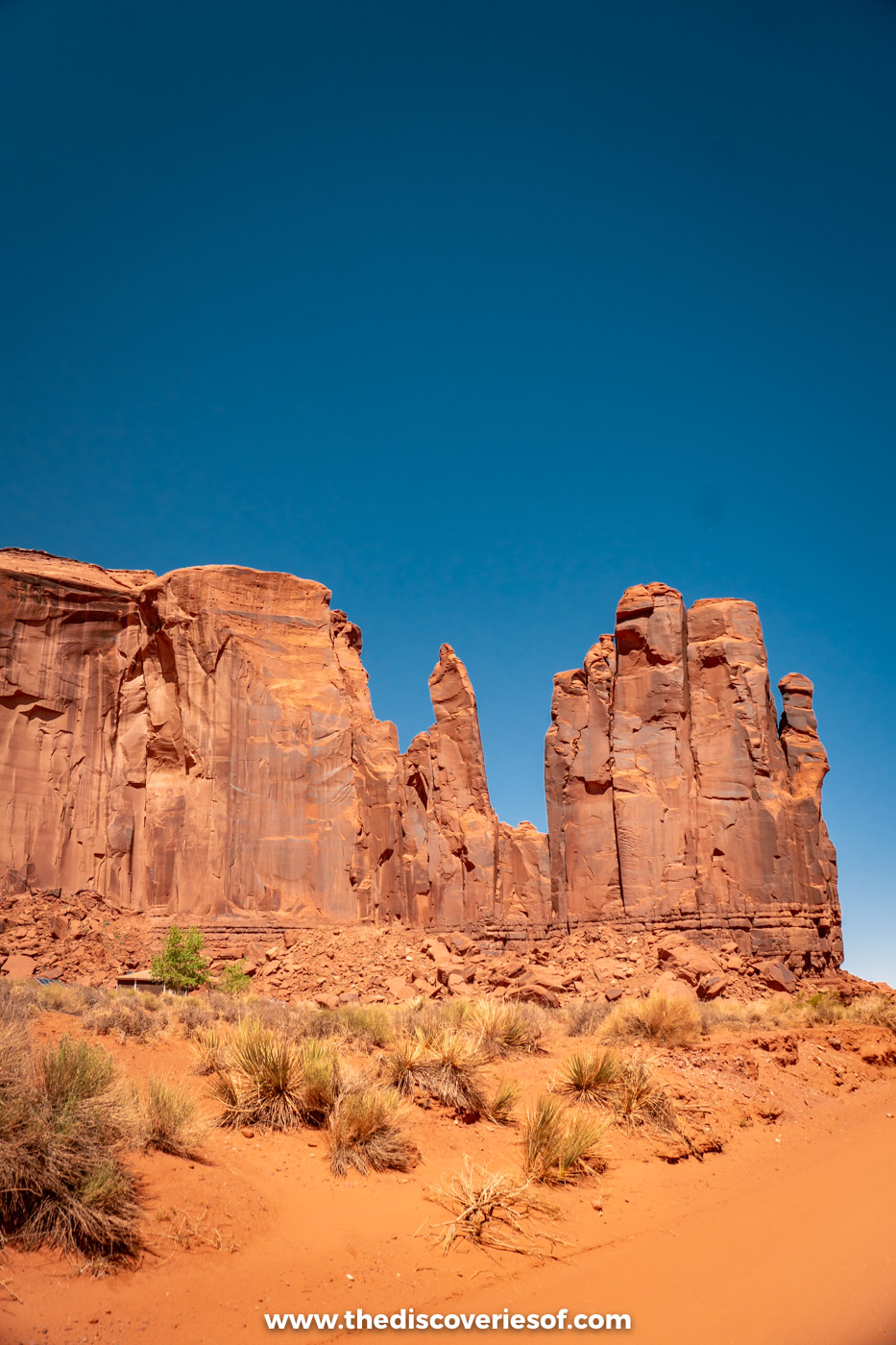 Jagged red sandstone towers above desert scrub along the Valley Drive in Monument Valley